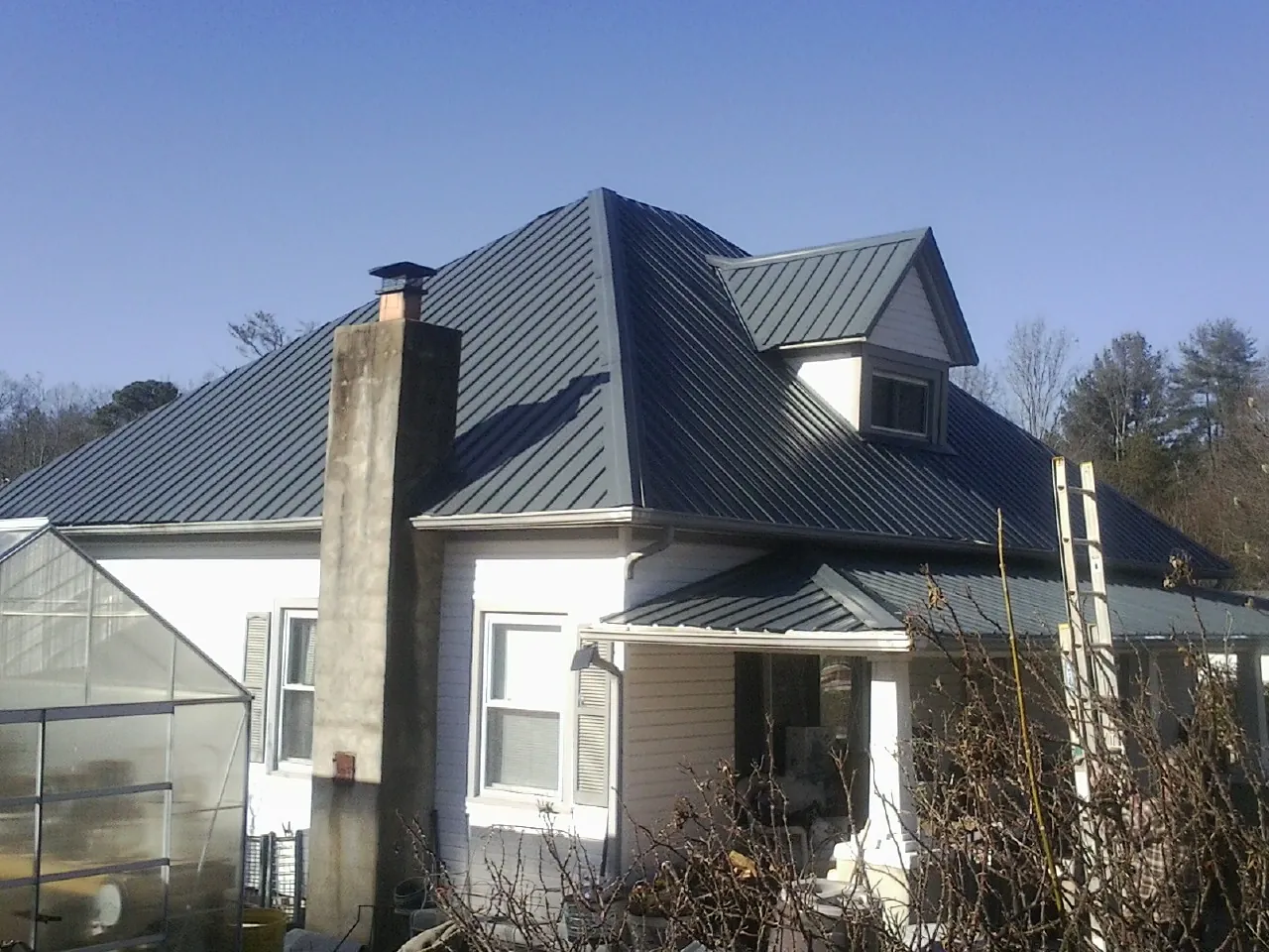 Dark blue standing seam metal roof on a white farmhouse with dormer — Slate & Tile Roof Repair by Roofing Brothers in Cave Spring