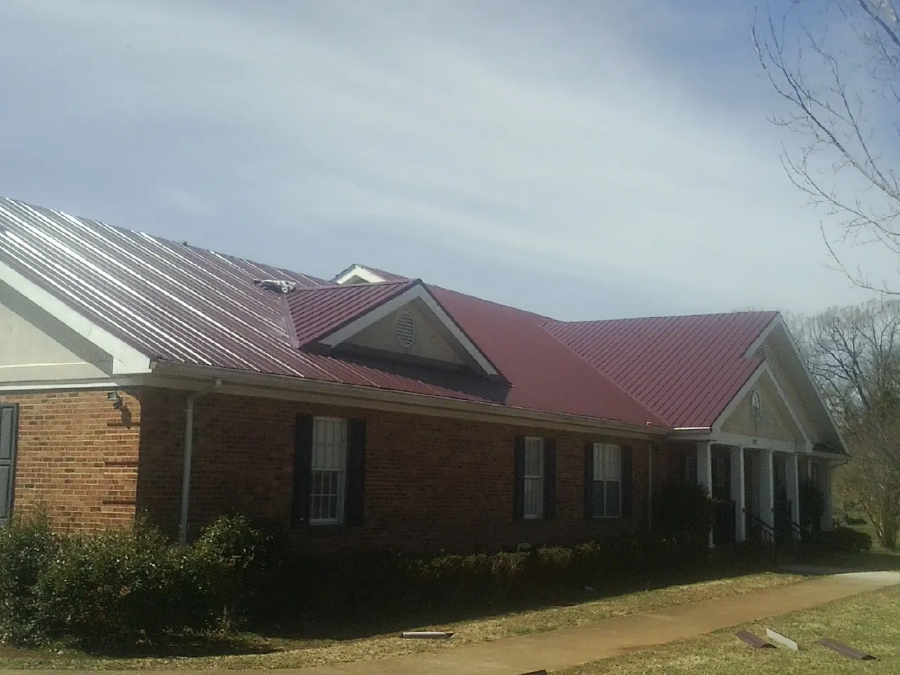 Red metal roof with gabled entries on a long brick building, from a Hail Damage Roof Repair job in Cave Spring