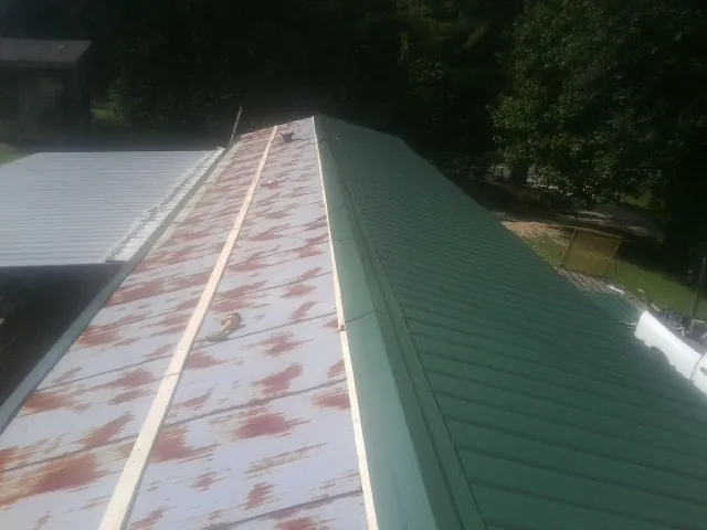 Old rusted panels beside newly installed green metal roofing — Wind Damage Roof Repair by Roofing Brothers in Cave Spring