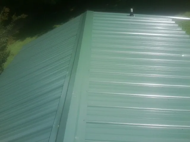 New green metal panels meeting at the ridge of a roof — Flat Roof Repair work by our crew in Cave Spring